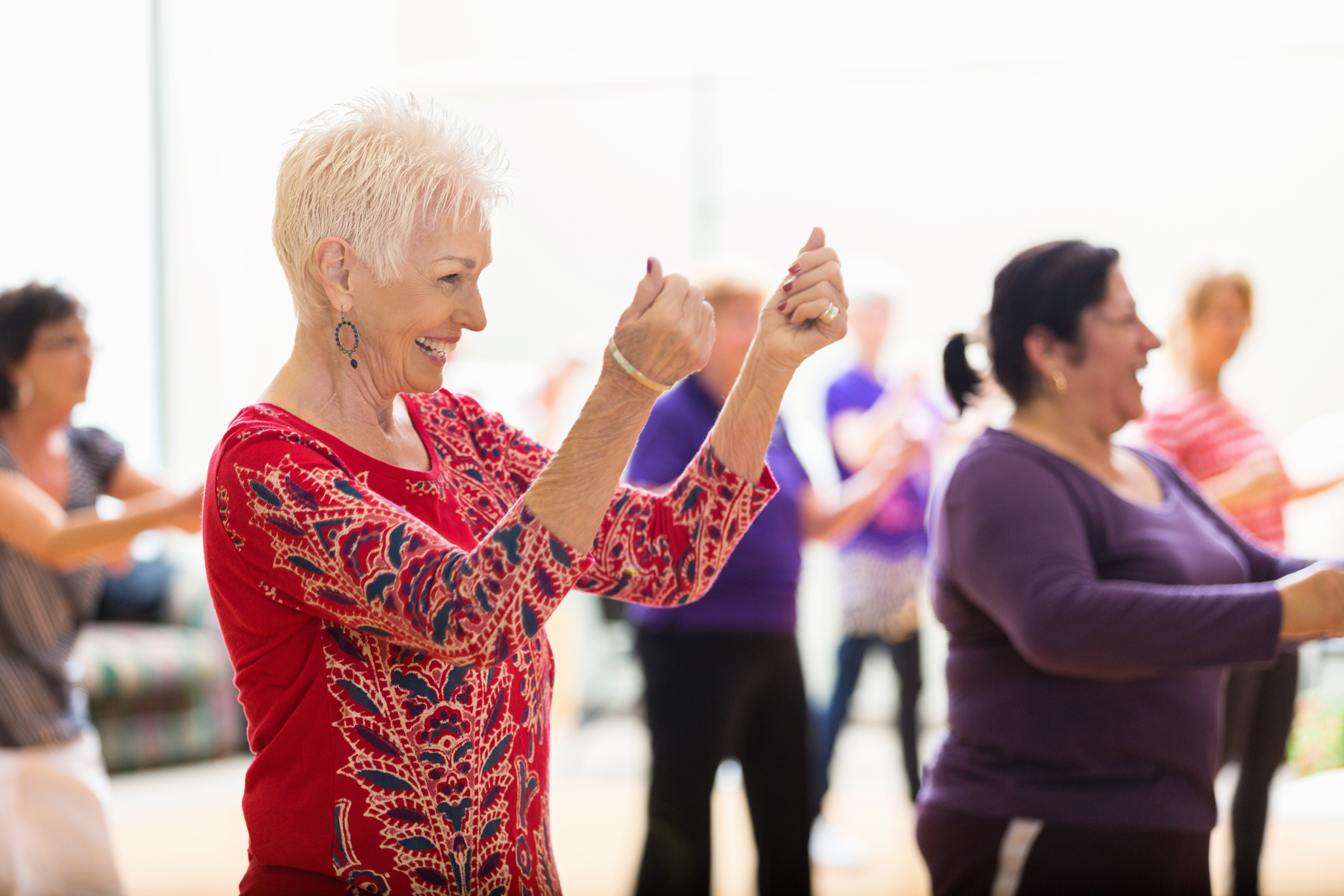Senior woman enjoys dance class Beautiful senior woman snaps her fingers as she learns new dance moves during dance class at her senior center. People are dancing in the background.