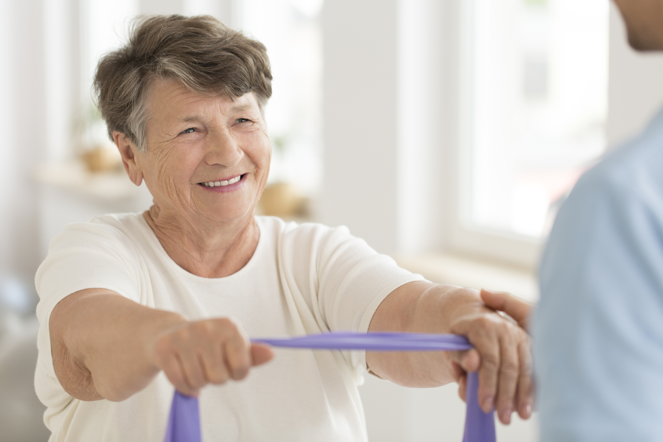 Smiling senior woman doing strength exercise with elastic tape during rehabilitation