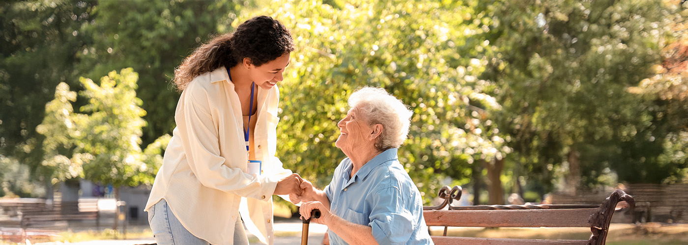 Senior woman sits in wheelchair smiling as younger female caregiver embraces her.