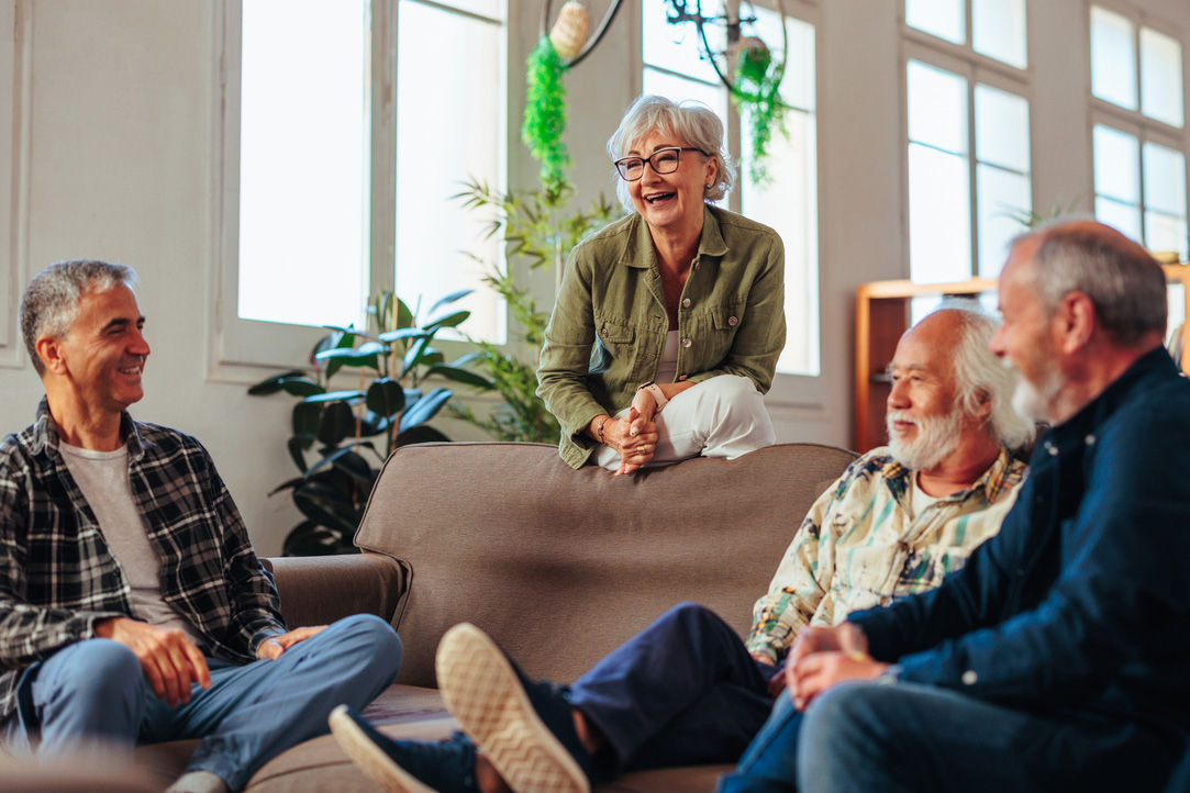 Four senior people talking and laughing while resting in living room. Monday Melodies