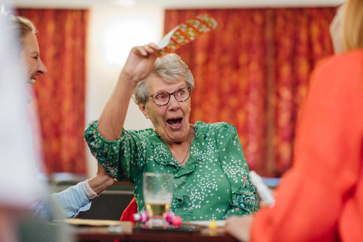A senior woman sitting with her daughter and playing bingo in a social club in Newcastle upon Tyne, England. She is holding up her bingo card and looking excited after getting the winning numbers.