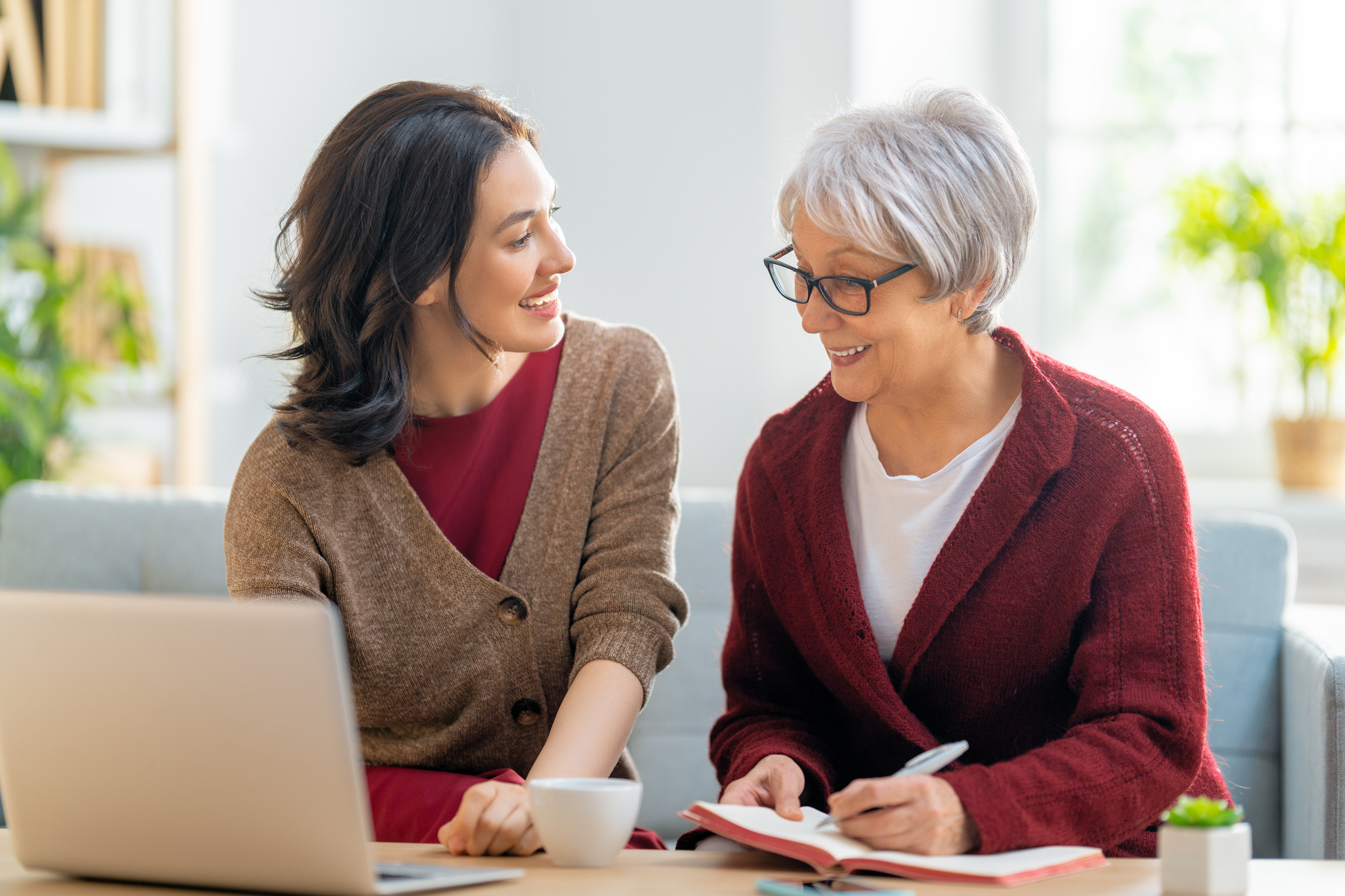 Two women, sitting on the sofa with a paper receipt, are calculating expenses, managing the family budget.